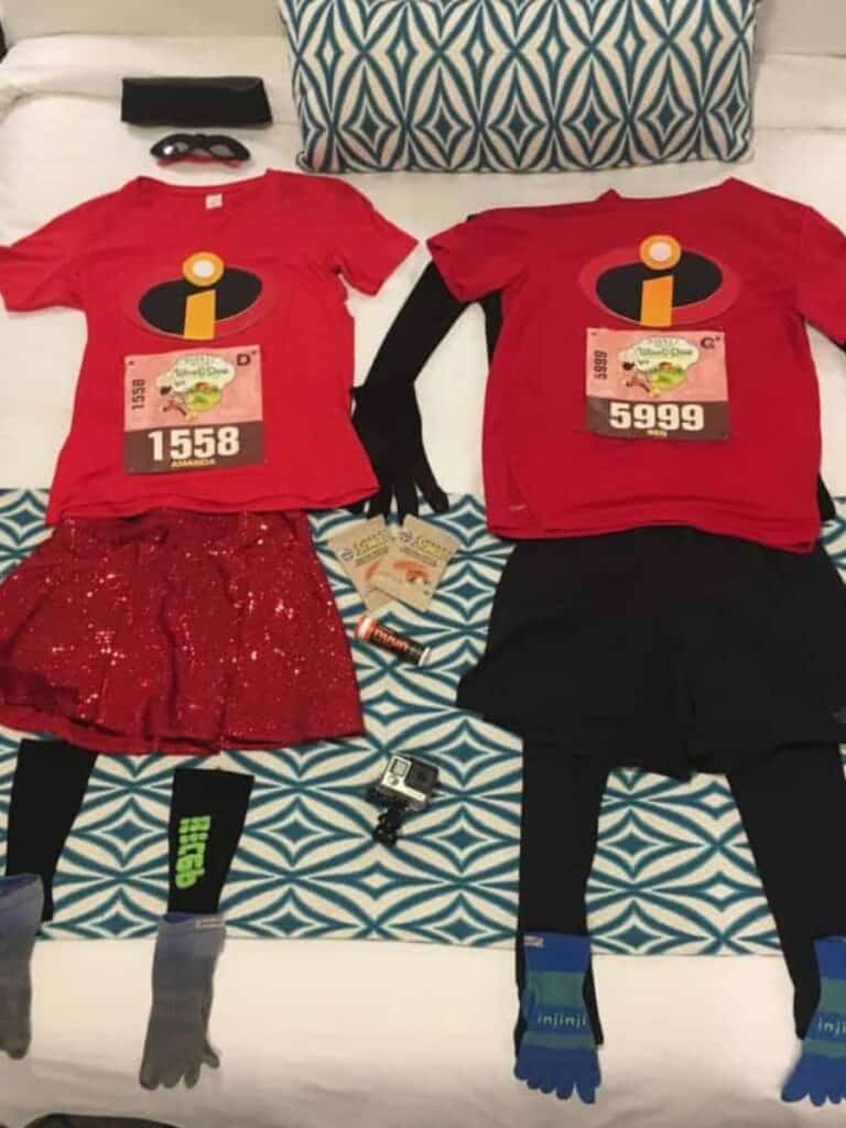Running clothes for two runners is laid out on a bed along with running fuel, hydration, and a GoPro camera. Laying out your clothes the night before a half marathon is a top tip for a successful race day.