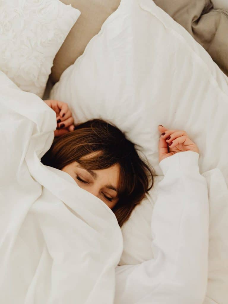 A woman sleeping in bed with the covers pulled halfway up her face. Sleep is important when tapering in running training cycles.