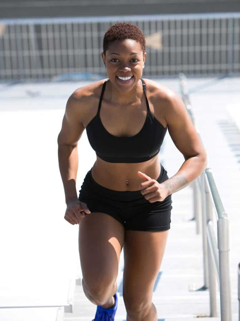 A female running is running up stadium stairs with a big smile on her face.