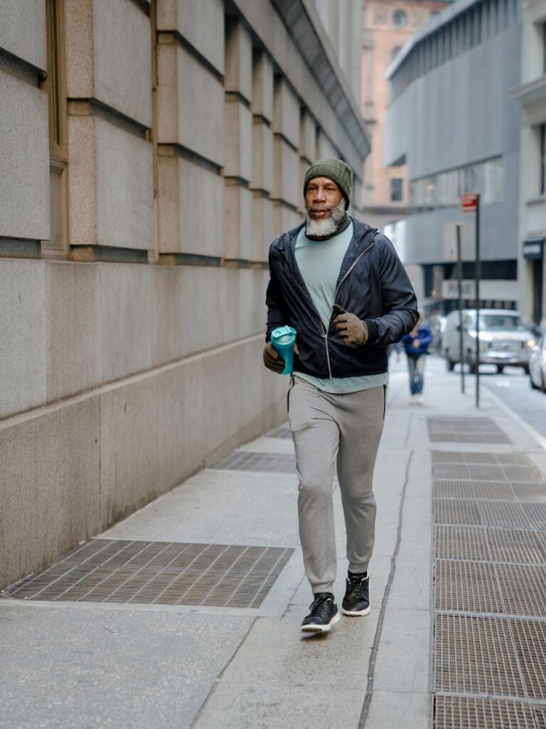 A man is running down a city street with his water bottle in his right hand.
