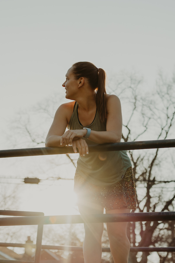 I'm leaning on a railing looking over my right shoulder while dressed in my running clothes.