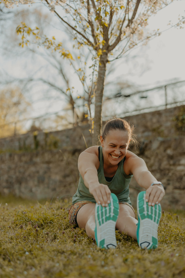 I'm sitting on the ground in my running clothes with a big smile from laughter on my face as I stretch forward over my legs to reach my toes. Running puns and jokes for runners are a great way to ease the running tension.