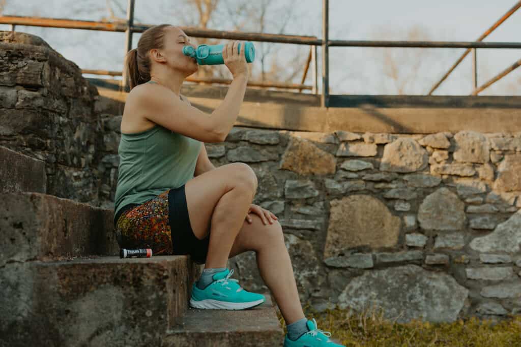 I'm sitting on steps next to a stone wall. I'm in my running clothes and drinking Nuun hydration sports drink. Staying hydrate is an important running tip for beginners.