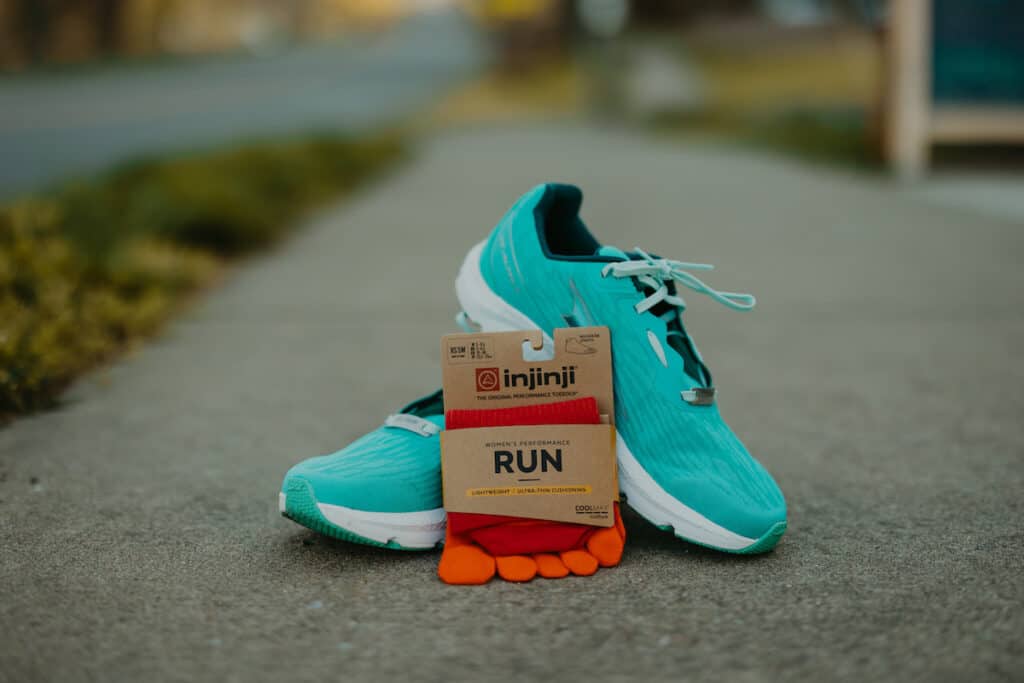 A pair of Altra Running shoes are stacked on one another. A pair of Injinji Run socks are leaned up against the Altra running shoes. Getting quality running gear is an essential running tip for beginners.