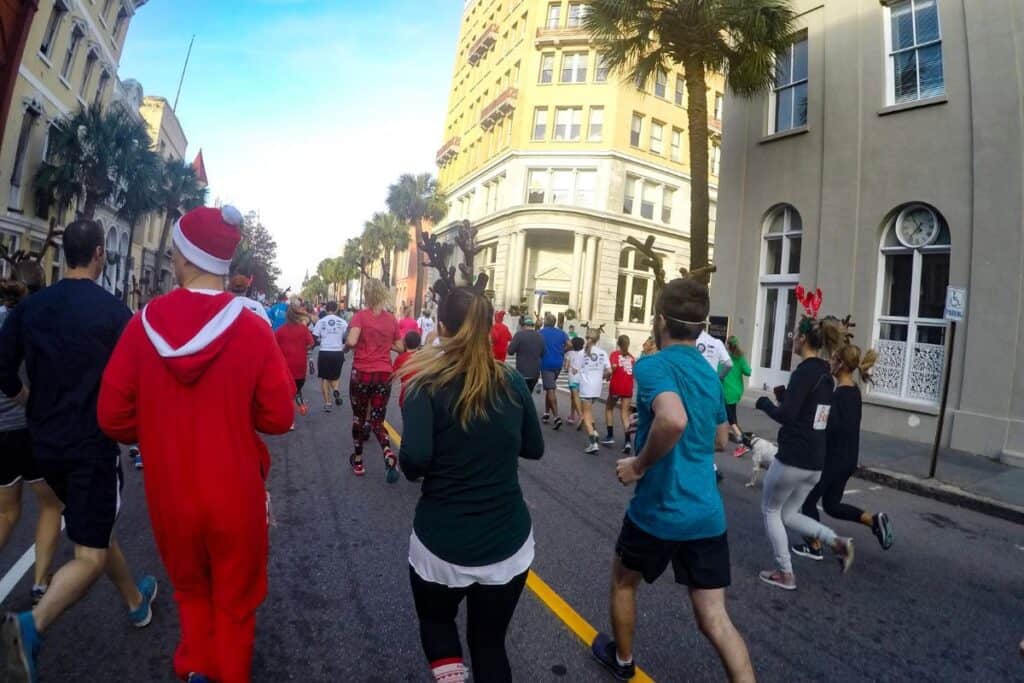 Many runners run through the streets of downtown Charleston, South Caroline for the annual Reindeer Run 5k in December 2017. One runner is wearing a red Santa Claus onesie, many other runners are wearing reindeer antlers.