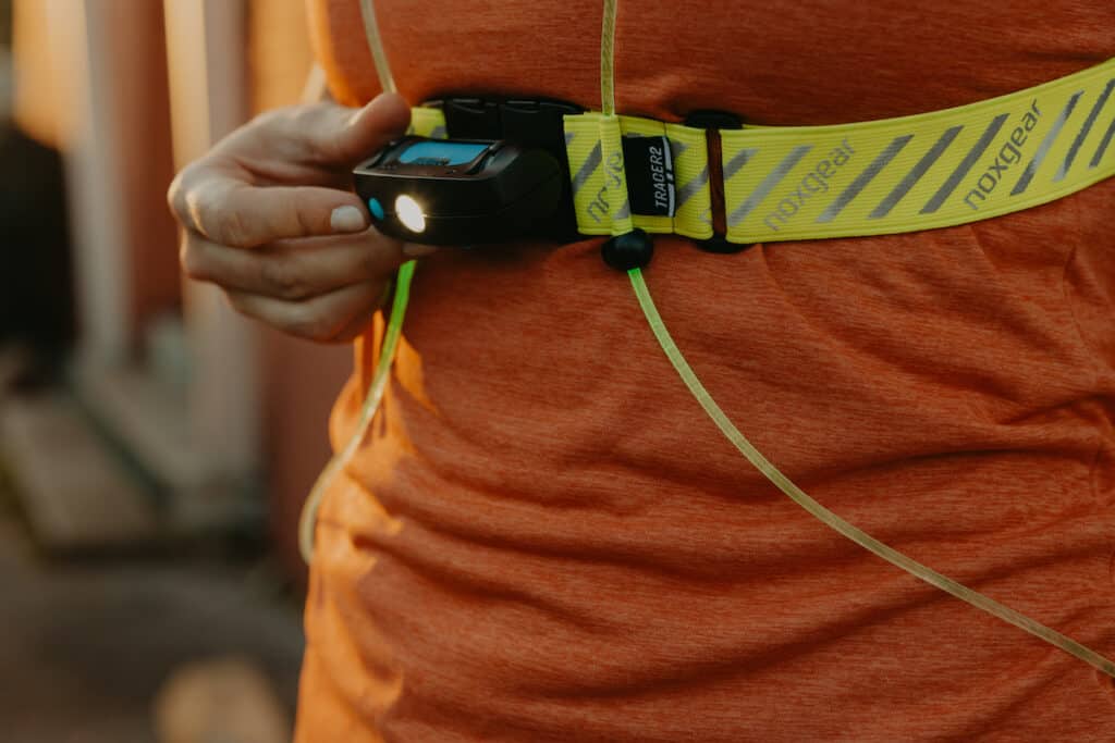 A close-up of my Tracer Lamp attached to my Noxgear Tracer2 running vest. My hand is sitting next to the on/off button and the light is turned on.