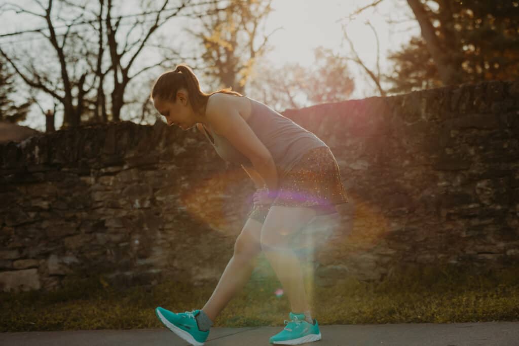 I am stretching my right hamstring by placing my heel on the ground, toes stretching upward, and leaning my upper body over the leg. I am preparing to run, wearing my running clothes in a park on a sunny day.