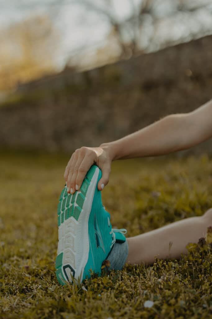 My right foot is in frame, wearing an Altra running shoes. My hand is reaching and grabbing my toes to stretch my leg muscles before running.