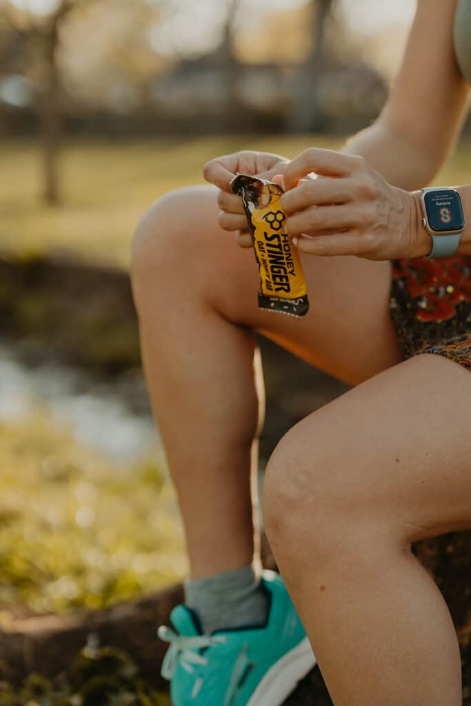 I'm sitting down on a tree stump, opening a Honey Stinger Oat + Honey Bar to help prepare my body to run.