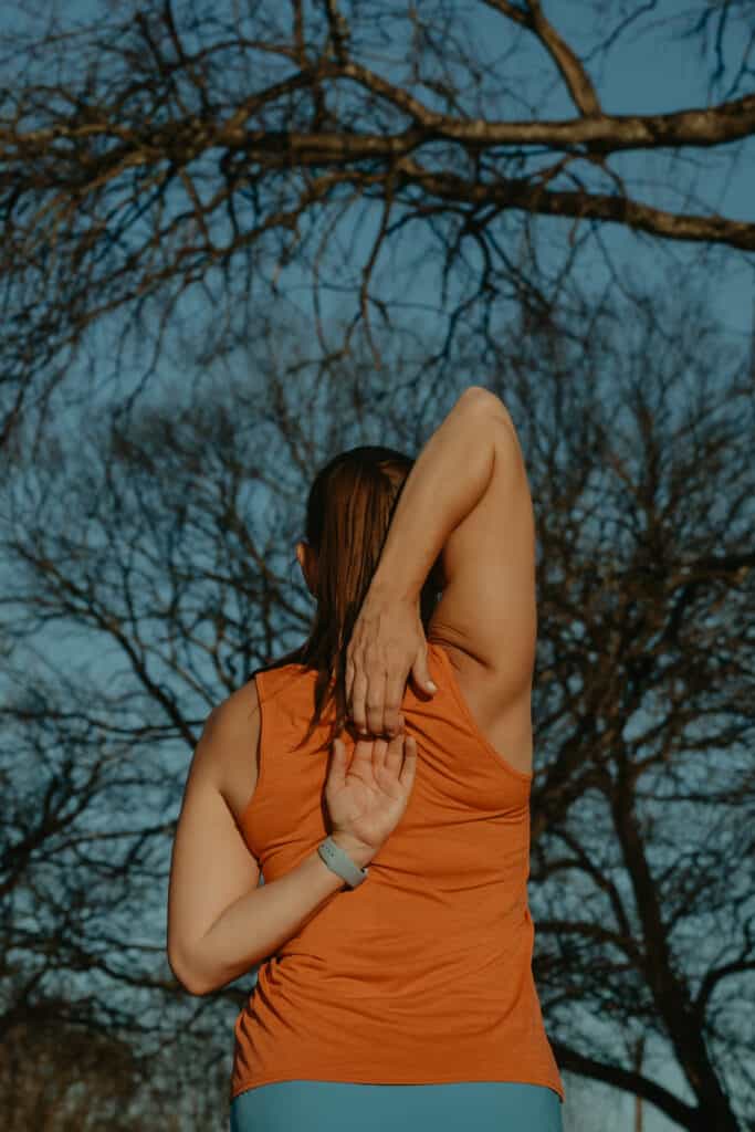 I am wearing my running clothes and stretching my arms behind my back to prepare for a run or walk.