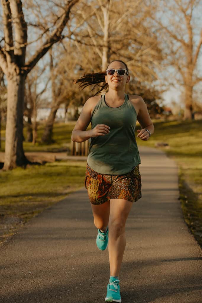 I'm running toward the camera on a running path in a park. I'm wearing my running clothes including a tank top and skirt and sunglasses. I have a smile on my face.