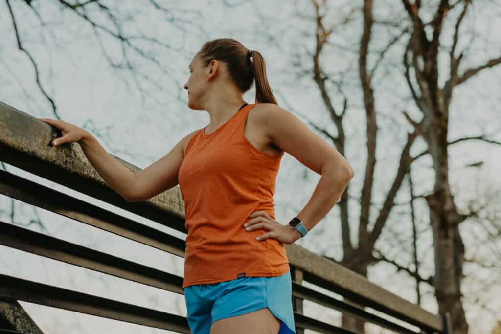 I'm standing on a walking bridge wearing my running clothes, looking off into the distance with one hand on my hip and one on the railing of the bridge.